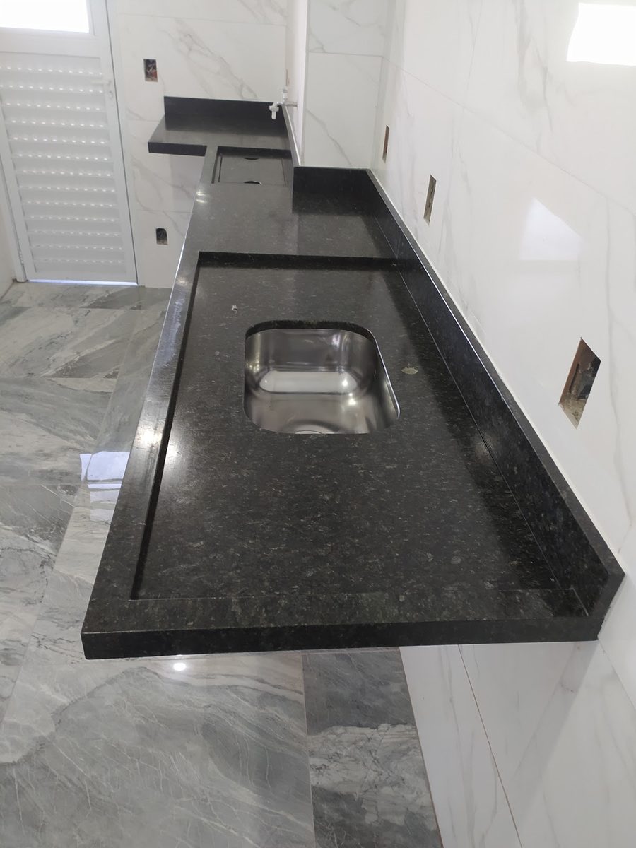 Bancada longa em granito preto com cuba de inox e parede em porcelanato marmorizado